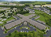 Thumbnail 7 of 15 - A large, multi-story building with a parking lot in front is surrounded by smaller buildings and greenery.