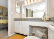 Thumbnail 25 of 32 - Model apartment bathroom with granite countertops, a large mirror, and ample lighting at The Oasis Daytona