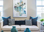 Thumbnail 5 of 8 - a living room with a couch and pillows and a painting on the wall flanked by windows