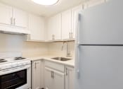 Thumbnail 11 of 26 - A white kitchen with a refrigerator, oven, and sink.