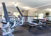 Thumbnail 18 of 33 - A gym with a row of exercise bikes and a bench with dumbbells on it.