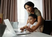Thumbnail 7 of 8 - a woman and a child looking at a laptop computer in front of a window
