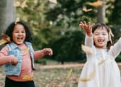 Thumbnail 4 of 8 - two young girls playing outside and tossing autumn leaves in the air