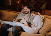 Thumbnail 1 of 8 - a man with a tv remote in his hand and woman sitting on a couch