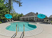 Thumbnail 7 of 28 - A swimming pool surrounded by trees and a building in the background.