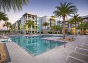 Thumbnail 15 of 44 - The swimming pool and large pool deck with towering palms and apartment homes at Residences at The Green in Lakewood Ranch
