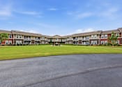 Thumbnail 9 of 15 - A large apartment complex with a parking lot in front.