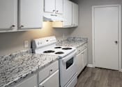 Thumbnail 3 of 8 - The Bluffs Kitchen with white stove, white cabinets and wood-style flooring at The Bluffs