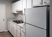 Thumbnail 4 of 8 - Fridge, white cabinets, and double stainless steel sink in apartment kitchen at The Bluffs
