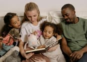 Thumbnail 1 of 8 - a family sitting on a couch reading a book to their children