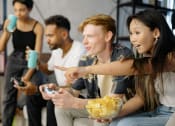 Thumbnail 5 of 8 - a group of people sitting on a couch playing video games and eating snacks