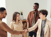 Thumbnail 6 of 8 - a diverse group of people standing in a leasing office with two people shaking hands