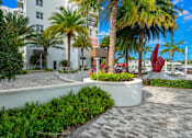 Thumbnail 33 of 40 - A sculpture of a red bird is in the foreground of a courtyard with palm trees and a white building in the background.