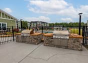 Thumbnail 14 of 197 - A stone fireplace with a grill on top is in the middle of a concrete patio at Foxwood Apartments, Raleigh-Durham, NC