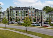 Thumbnail 184 of 197 - A green and beige apartment building with a parking lot in front at Foxwood Apartments, Raleigh-Durham, North Carolina