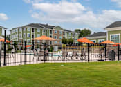 Thumbnail 16 of 197 - A black fence surrounds a pool area with orange umbrellas at Foxwood Apartments, Raleigh-Durham, NC, 27616