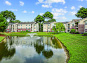 Thumbnail 26 of 31 - A pond with a fountain in the middle of a grassy area in front of apartment buildings.