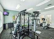 Thumbnail 17 of 31 - A gym with a variety of equipment including a treadmill, weights, and a television.