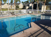 Thumbnail 9 of 15 - Community pool with sundeck, lounge chairs, with lake view surrounded by white metal fence with palm trees and building exteriors in the background