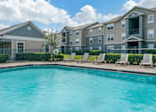 Thumbnail 2 of 24 - Swimming pool with lounge seating and apartment building exterior in the background