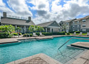 Thumbnail 1 of 24 - Swimming pool with lounge seating surrounded by native landscaping and apartment building exterior in the background