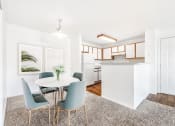 Thumbnail 18 of 25 - Model Apartment with Dinette Table in Front of Framed Wall Art Next to Open Kitchen with White Cabinets with Wood Accents and White Appliances