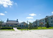 Thumbnail 6 of 24 - Sand Volleyball Court with Net and Sidewalk Through Shrubs with Leasing Office in the Background