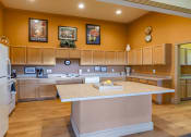 Thumbnail 24 of 27 - Clubhouse kitchen with wood cabinetry, large island, white appliances and coffee maker with wood style flooring
