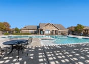 Thumbnail 19 of 27 - Swimming pool with large tanning deck, lounge chairs, round table and chairs with clubhouse exterior in background and native landscape