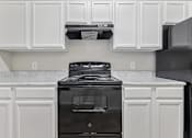Thumbnail 2 of 27 - A black stove in a kitchen with white cabinets.