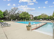 Thumbnail 1 of 33 - A large outdoor swimming pool surrounded by trees and a building in the background.