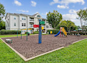 Thumbnail 13 of 29 - A playground with a slide, swings, and a seesaw in front of a building.