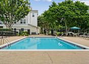 Thumbnail 5 of 29 - A swimming pool in a residential area with a house and trees in the background.