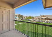 Thumbnail 17 of 27 - A balcony with a white door and a black railing overlooking a green lawn and houses.