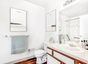 Thumbnail 23 of 25 - Model Bathroom with White Counters, White Cabinets with Wood Accents and Towel Holder Under Framed Art