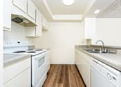 Thumbnail 8 of 17 - A white kitchen with a stove, sink, and cabinets.