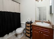 Thumbnail 21 of 36 - A bathroom with a white toilet, a brown cabinet, and a black shower curtain.
