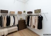 Thumbnail 8 of 27 - A white closet with clothes hanging and a bench underneath.