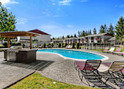 Thumbnail 7 of 23 - Sparkling Swimming Pool with a Spa and Lounge Chairs in Front of the Resident Grilling Station at Pinewood Square Apartment Homes, Washington