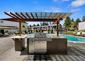 Thumbnail 9 of 23 - Decadent Resident Outdoor Kitchen with a Shaded Wooden Pergola Next to the Sparkling Swimming Pool at Pinewood Square Apartment Homes, Lynnwood, WA