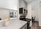 Thumbnail 18 of 23 - Cozhy Kitchen with Stainless Steel Appliances, Plank Flooring, Spacious Cabinetry, and View of the Living Area at Pinewood Square Apartment Homes, Lynnwood, WA