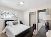 Thumbnail 15 of 23 - a bedroom with a bed and a dresser with a washer and dryer at Pinewood Square Apartment Homes, Lynnwood, Washington 98087
