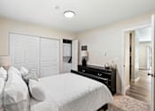 Thumbnail 19 of 23 - Cozy Bedroom with White Bed facing the Dresser and Large Closet doors, and overhead Lighting at Pinewood Square Apartment Homes, Lynnwood, 98087