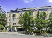 Thumbnail 13 of 27 - an apartment building with yellow and blue siding and a tree in front of it at Sir Gallahad Apartment Homes, Washington