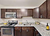 Thumbnail 4 of 23 - A kitchen with a granite counter top and dark wood cabinets at MainCentre, Northville