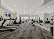 Thumbnail 26 of 34 - a gym with treadmills and other exercise equipment in a large room with windows at Cidermill Village Apartments in Rochester Hills, MI 