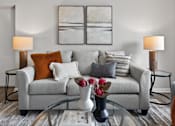 Thumbnail 2 of 16 - A grey couch with pillows and a vase of flowers on a glass table.