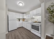 Thumbnail 6 of 16 - A kitchen with white appliances and wooden floors.