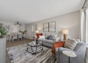 Thumbnail 3 of 16 - A living room with a grey couch, a coffee table, and a dining table.