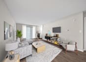 Thumbnail 6 of 23 - A modern living room with a grey sofa, a wooden coffee table, a white armchair, and a TV on the wall.